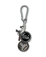 Keychain with 'Bada Bing' bottle cap charm and gun charm on a white background