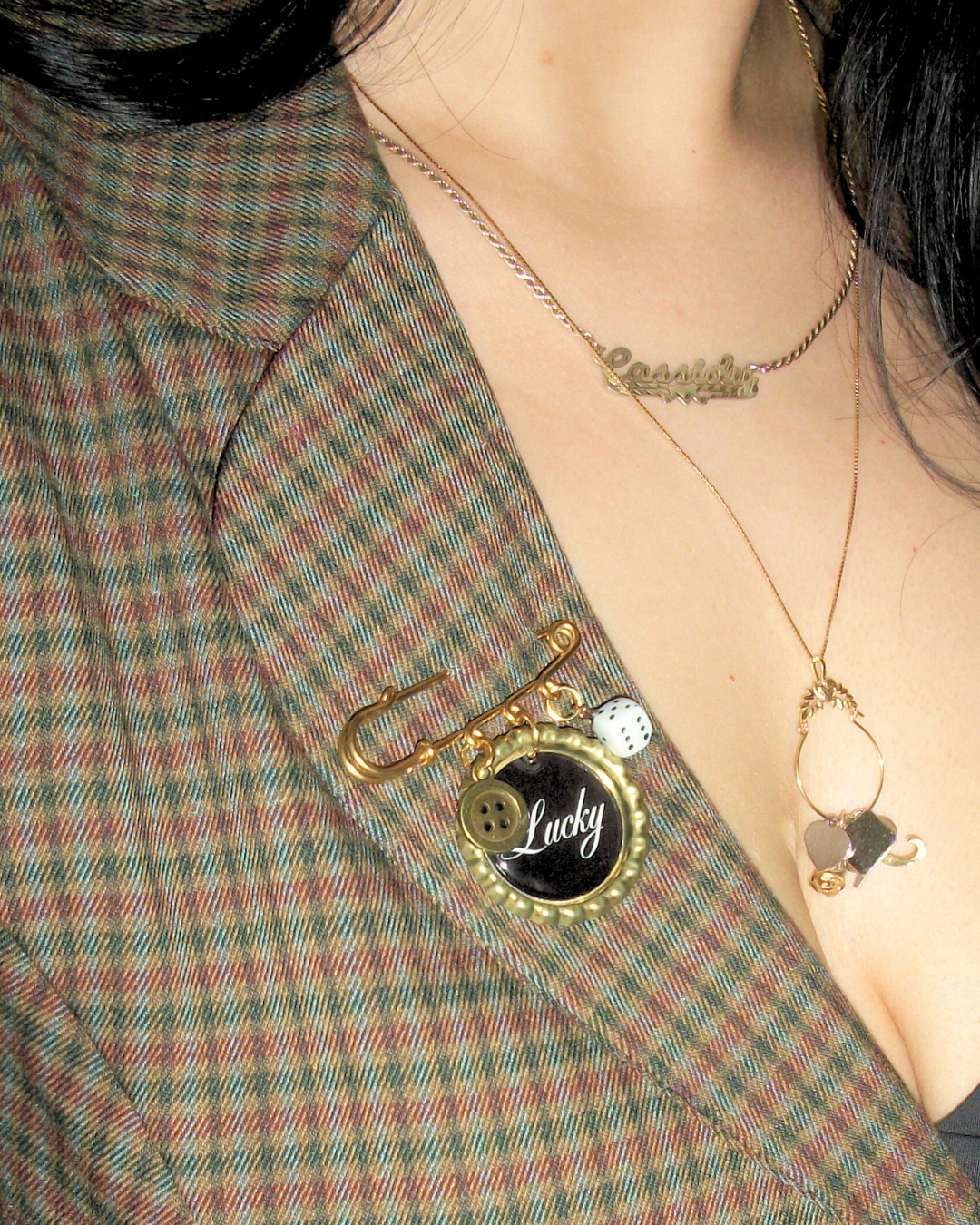 Close-up of a person wearing a gold 'Lucky' brooch on a plaid jacket.