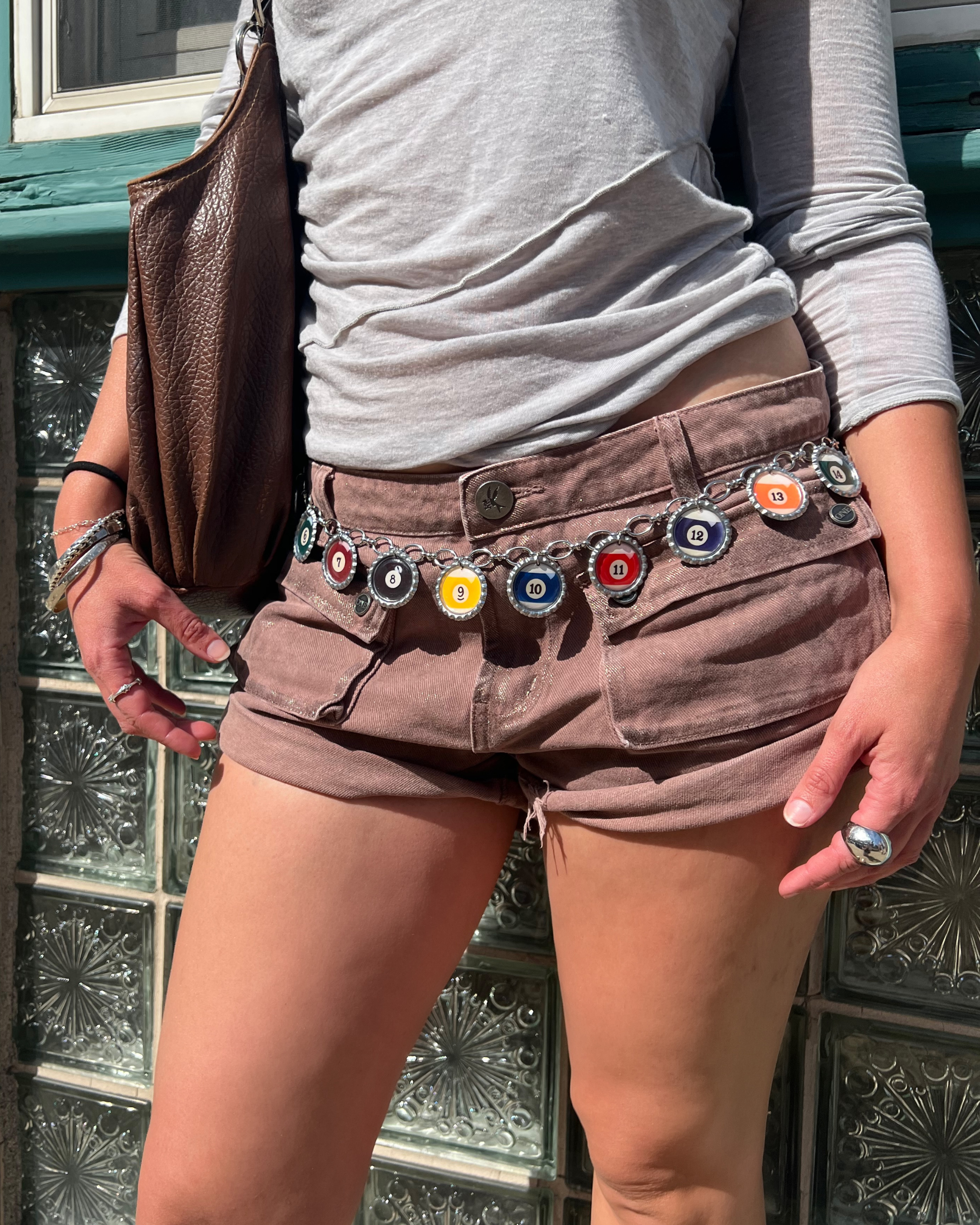 Person wearing brown shorts with decorative belt and gray shirt against a glass block wall.