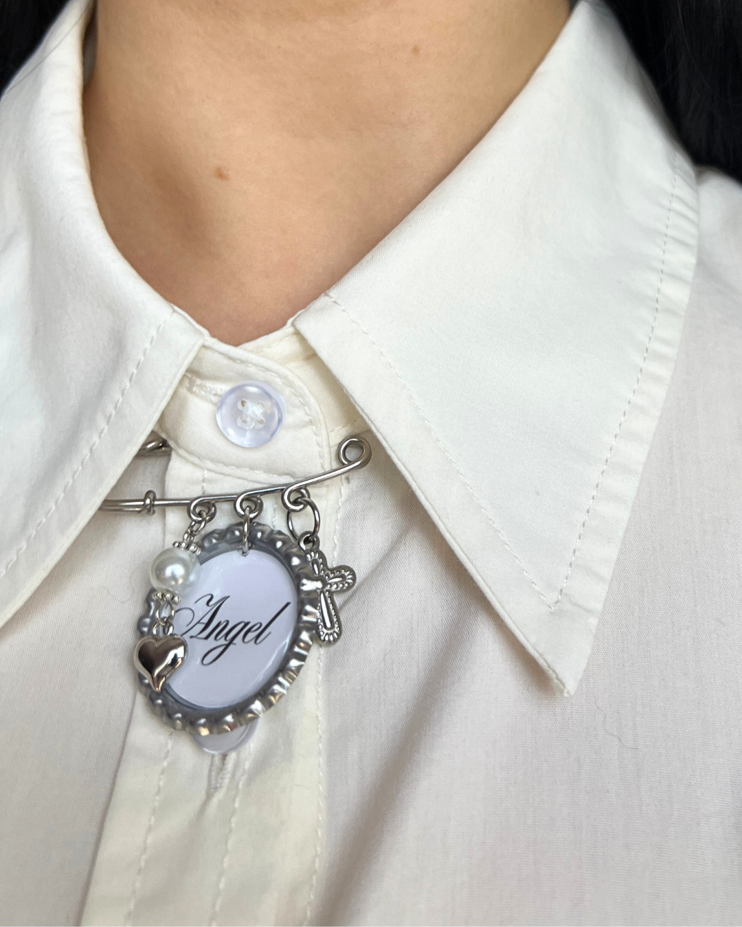Close-up of a white shirt with a decorative brooch featuring the word 'Angel'.