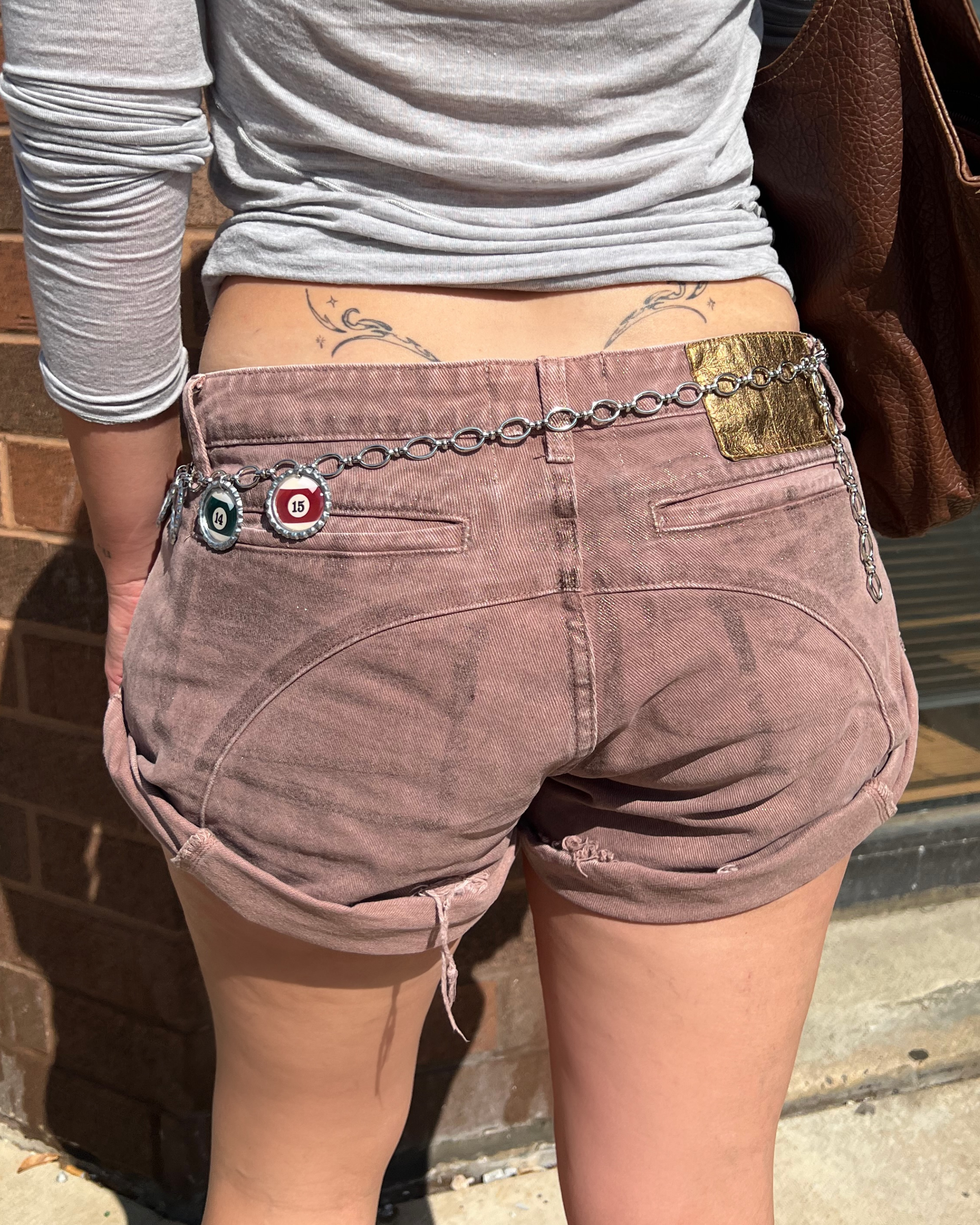 Person wearing brown shorts with a chain belt featuring a bottle cap charm.
