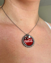Necklace with a Coca-Cola bottle cap pendant on a person's neck.
