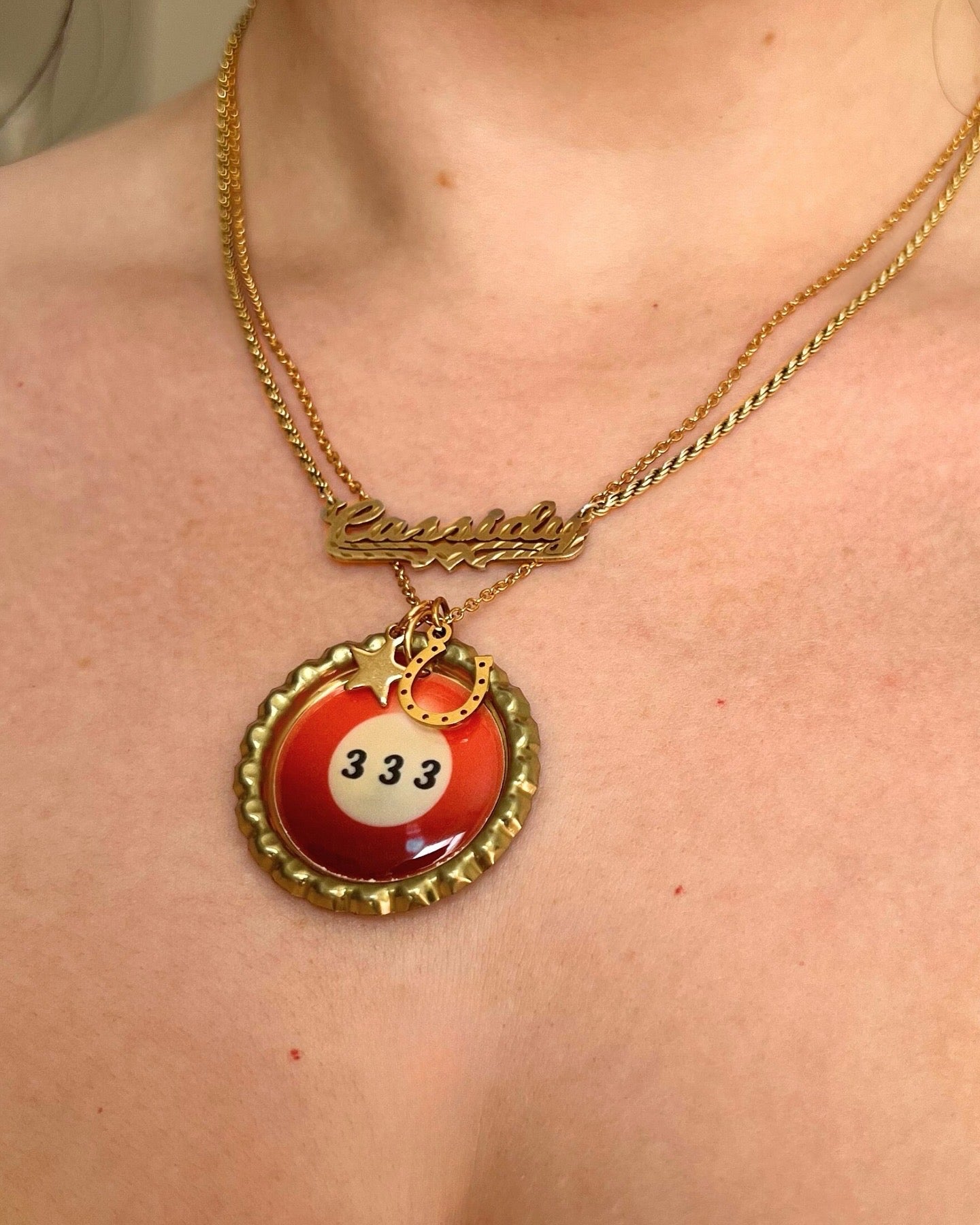 Gold necklace with a red billiard ball charm on a person's chest.