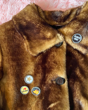 Brown fur coat with decorative buttons on a pink textured background