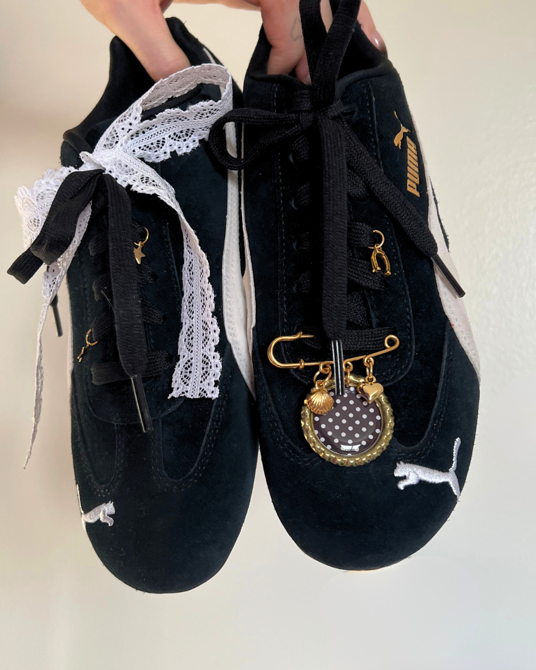 Black sneakers with decorative laces and charms on a plain background