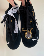 Black sneakers with decorative laces and charms on a plain background
