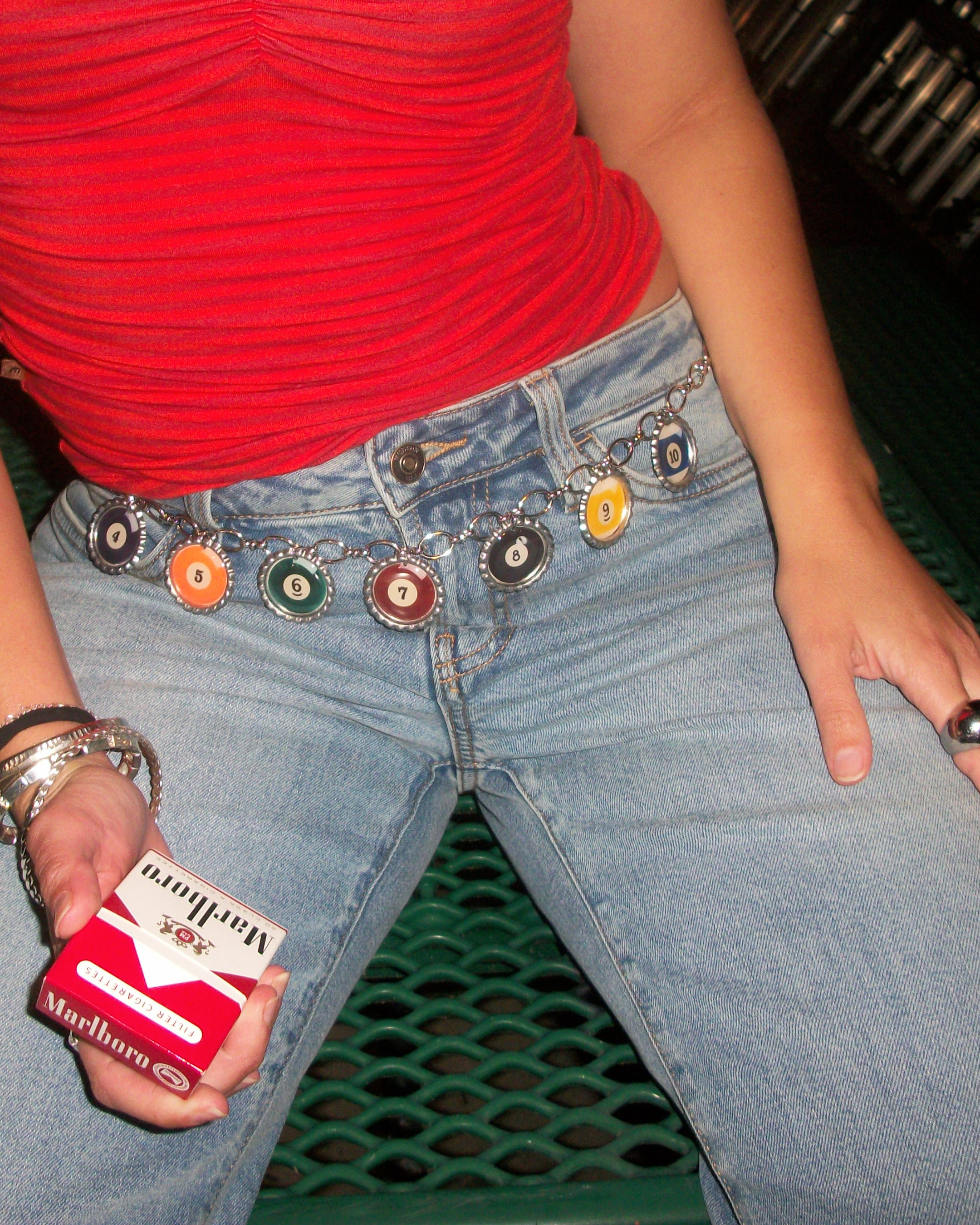 Person wearing a red top and blue jeans with a chain belt , holding a cigarette pack.