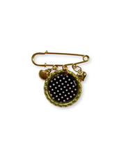 Gold brooch with black polka dot design on a white background