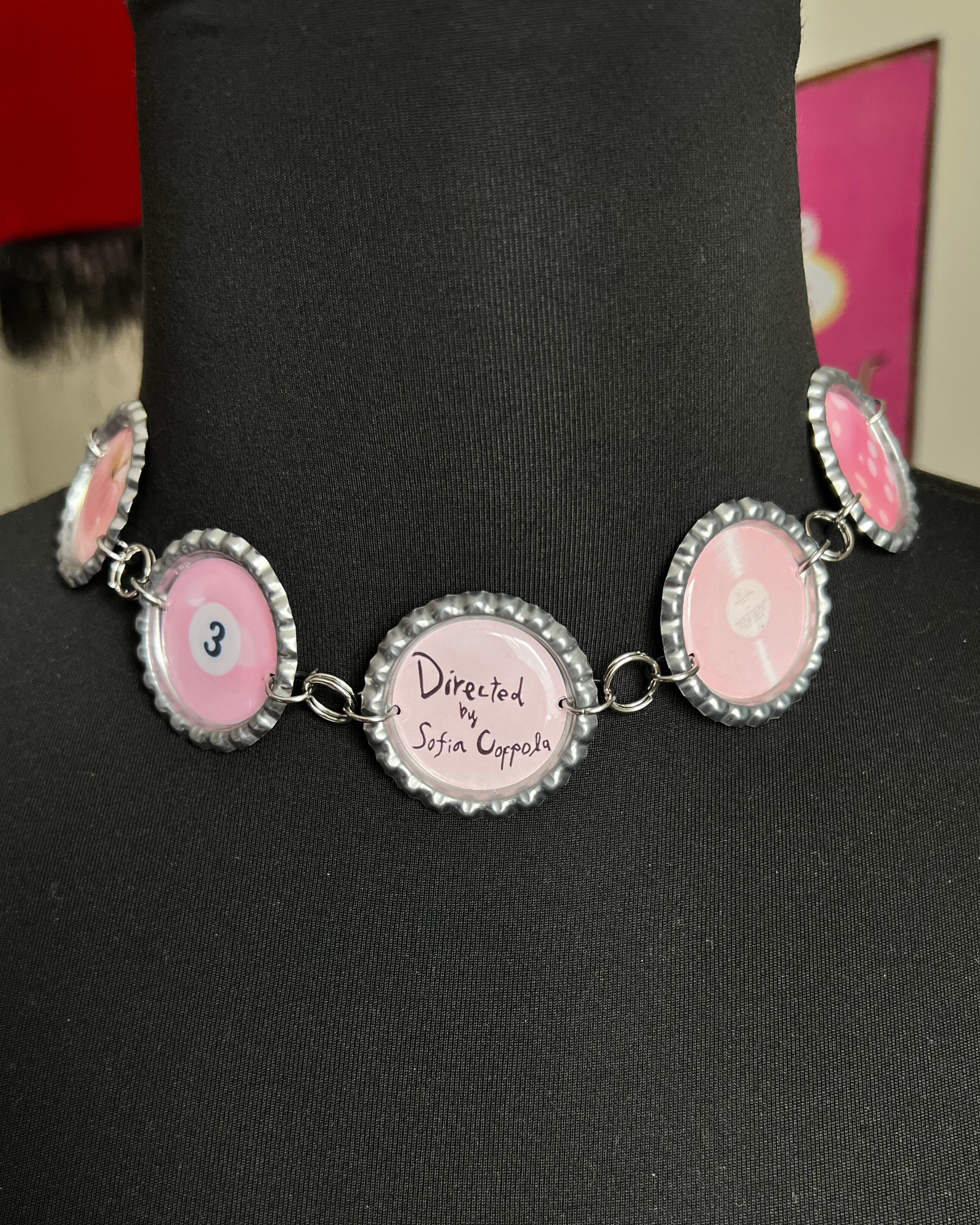 Necklace with pink bottle cap pendants on a black mannequin