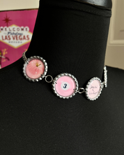 Bracelet with pink and silver charms on a black surface with Las Vegas sign in the background