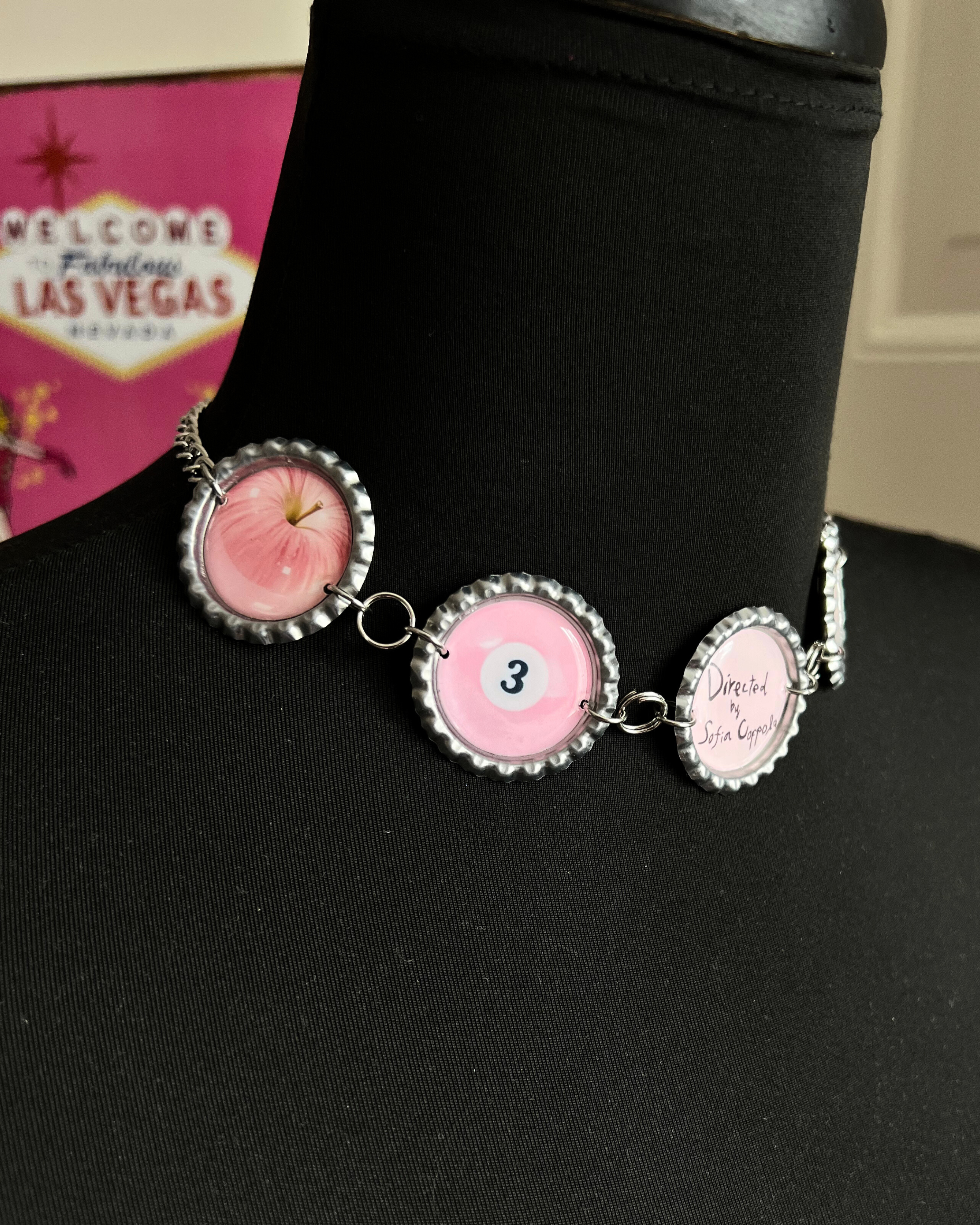 Bracelet with pink and silver charms on a black surface with Las Vegas sign in the background